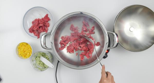 Al suono di Audiotherm, abbassare il calore e rosolare la carne di manzo. Aggiungere il trito di cipolla e i cubetti di peperone.